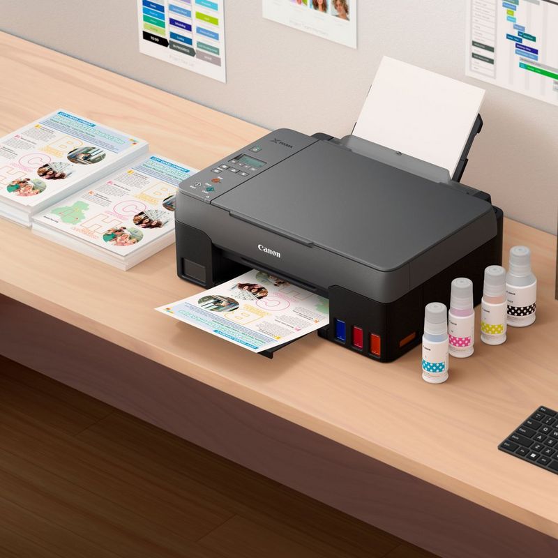 Canon PIXMA G2420 Colour 3-in-1 Refillable MegaTank Printer Kept On A Table Along With Printed Paper And Inks