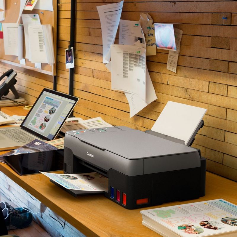 Canon PIXMA G2420 Colour 3-in-1 Refillable MegaTank Printer Kept On A Office Table Beside A Laptop With Paper Tray Out And Paper Support
