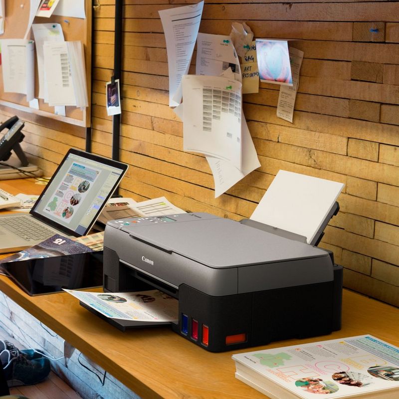 Canon PIXMA G2460 Colour 3-in-1 Refillable MegaTank Printer Kept On A Office Table Beside A Laptop With Paper Tray Out And Paper Support