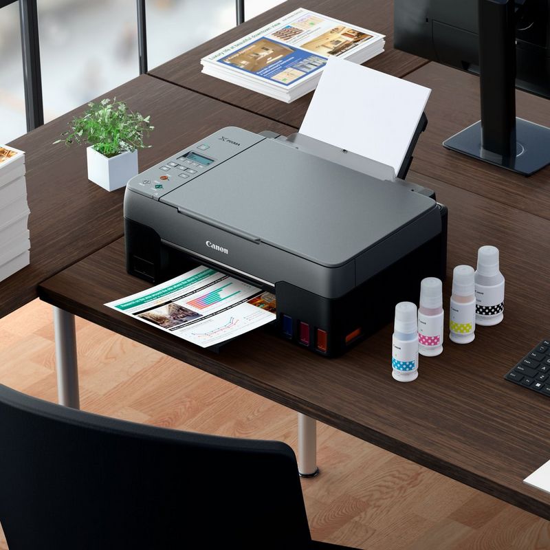 Canon PIXMA G3560: impresora MegaTank 3 en 1 inalámbrica en color con depósitos de tinta rellenable Sobre una mesa con la bandeja de papel abierta y un soporte de papel junto con tintas
