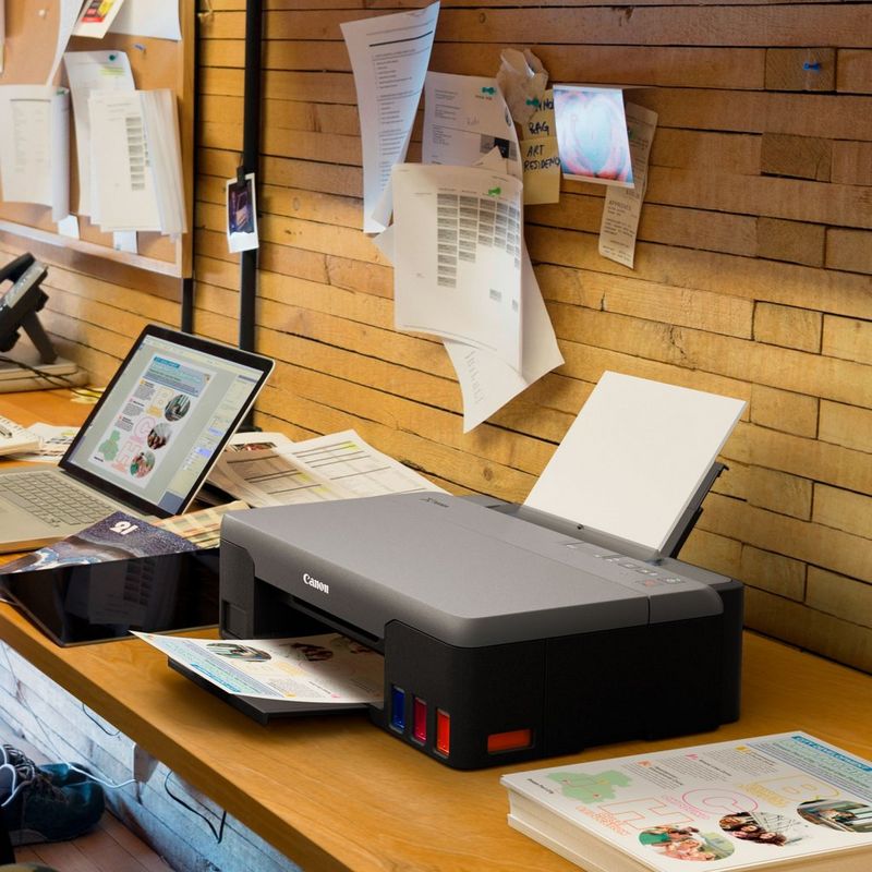 Canon PIXMA G1420 Colour Refillable MegaTank Printer Kept On A Office Table Beside A Laptop With Paper Tray Out And Paper Support