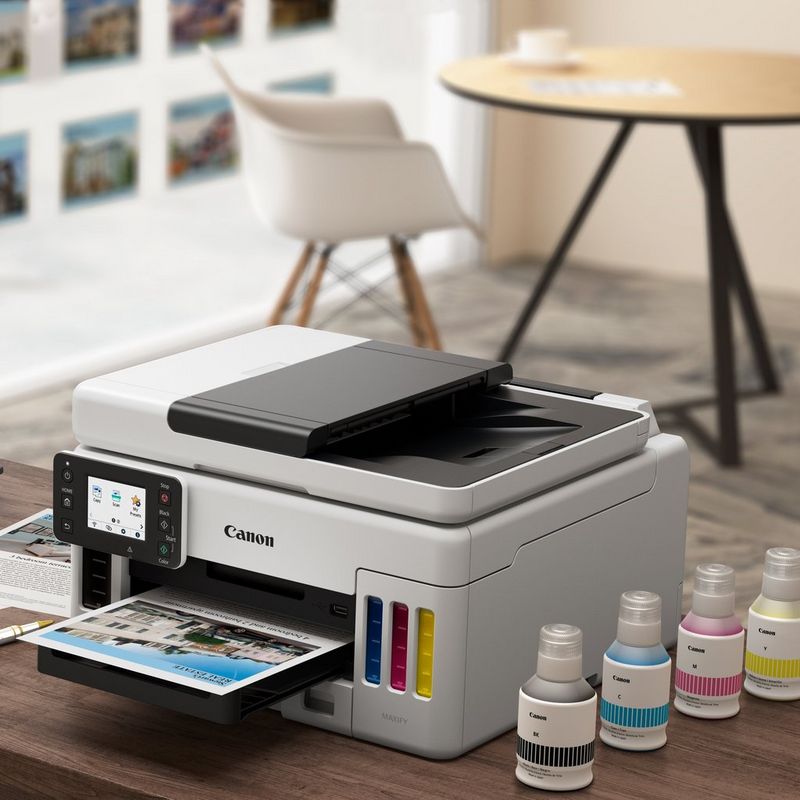 Canon MAXIFY GX6040 Wireless Colour 3-in-1 Refillable MegaTank Inkjet Printer Kept On A Table With Paper Tray Out Along With Ink Bottles