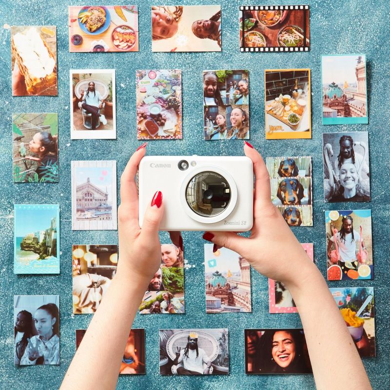 Canon Zoemini S2 Instant Camera Colour Photo Printer, Pearl White Printer displayed in hand with photos in the background