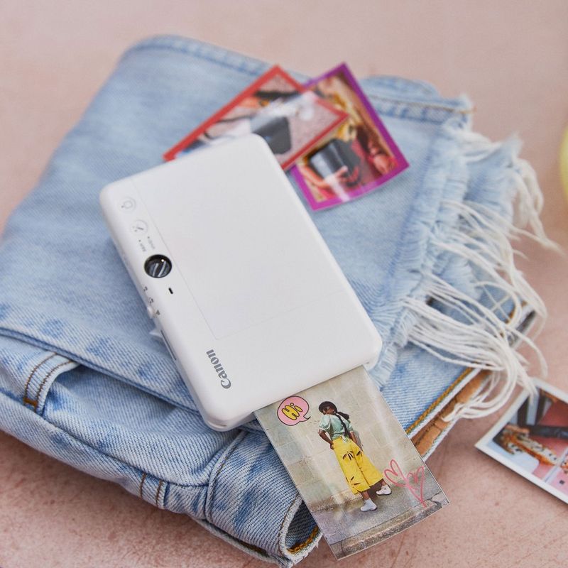 Canon Zoemini S2 Instant Camera Colour Photo Printer, Pearl White Printer kept on a pair of jeans with printouts