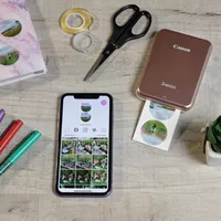 Canon ZINK™ Fotopapier mit vorgestanzten runden Stickern mit 33 mm Durchmesser, 20 Blatt Produkt Bei Verwendung auf einem Tisch neben einem Canon Zoemini Drucker und einem Smartphone
