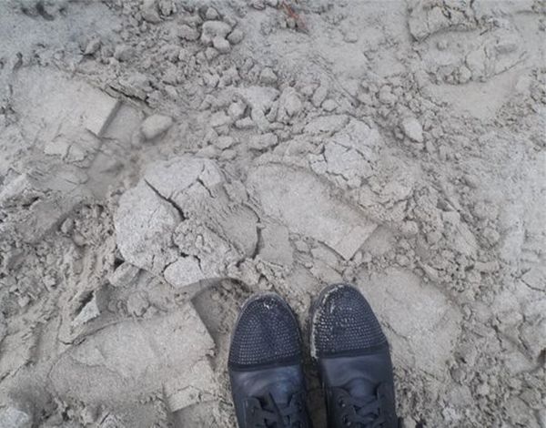 Feet in black shoes, stood on a dusty clay surface.