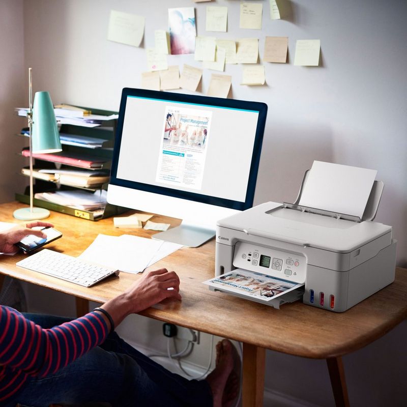 Canon PIXMA G3571 Wireless Colour 3-in-1 Refillable MegaTank Printer, White Product kept on Office Desk with a women holding a phone