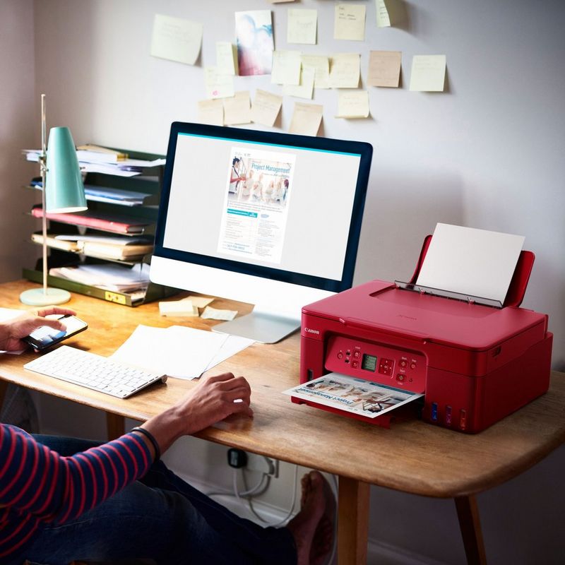 Canon PIXMA G3572 Wireless Colour 3-in-1 Refillable MegaTank Printer, Red Product kept on Office Desk with a women holding a phone