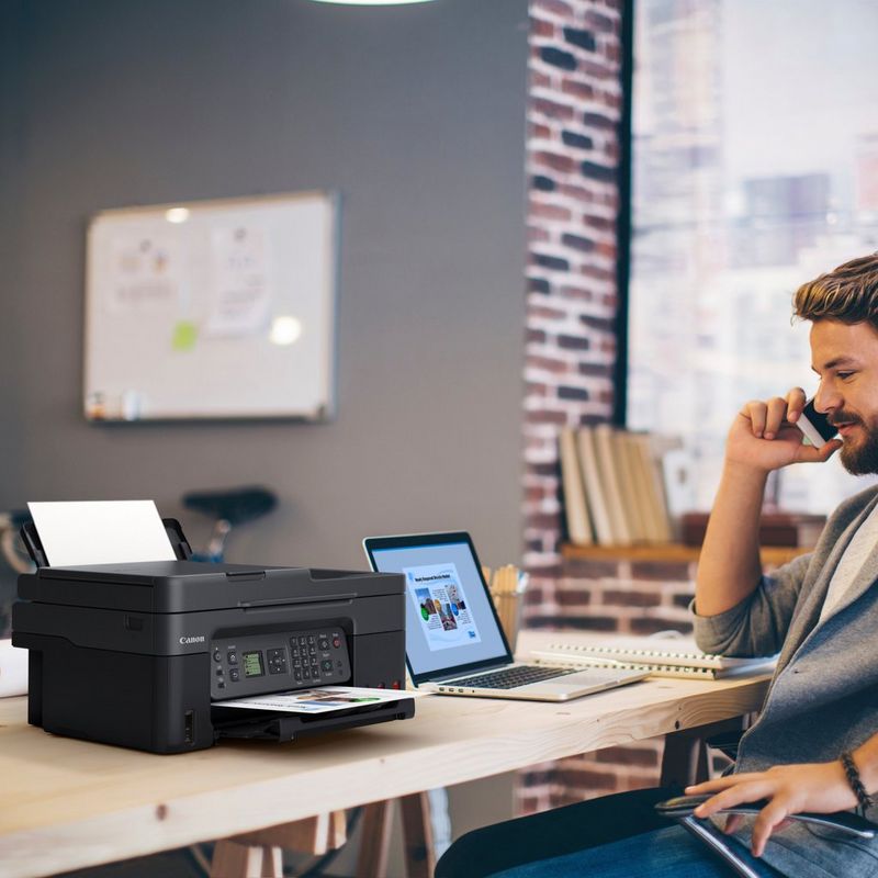 Canon PIXMA G4570: impresora multifunción inalámbrica MegaTank de inyección de tinta color con depósitos de tinta rellenables Producto en el escritorio de una oficina junto a un hombre hablando por teléfono