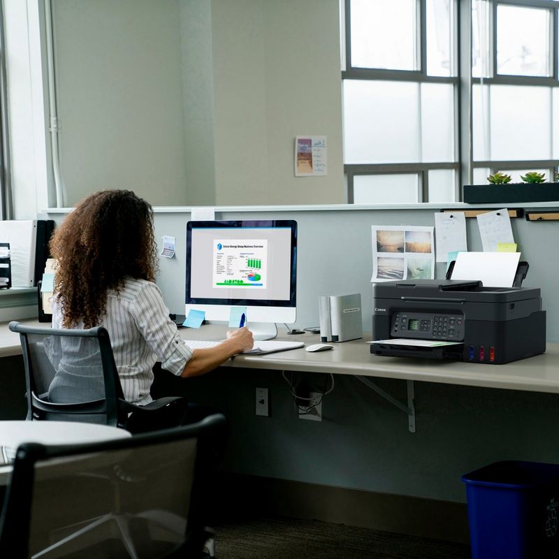 Canon PIXMA G4570: impresora multifunción inalámbrica MegaTank de inyección de tinta color con depósitos de tinta rellenables Producto en el escritorio de una oficina junto a una mujer trabajando en un ordenador