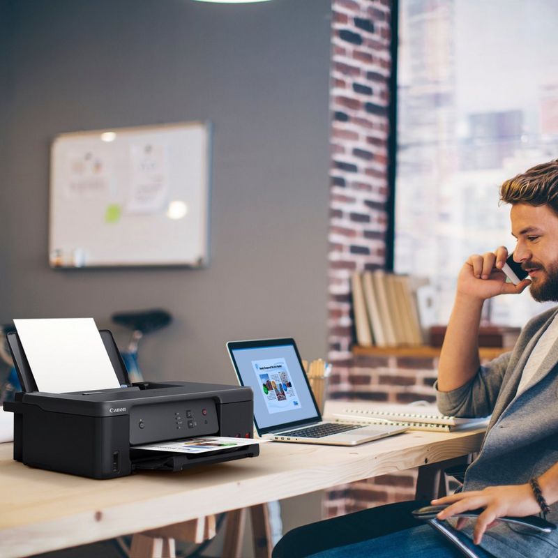 Imprimante MegaTank rechargeable couleur Canon PIXMA G1530 Produit posé sur un bureau avec un homme parlant au téléphone