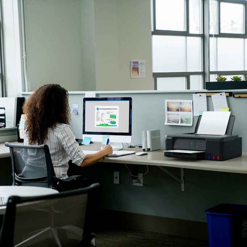 Imprimante MegaTank rechargeable couleur Canon PIXMA G1530 Produit posé sur un bureau avec une femme travaillant sur un ordinateur