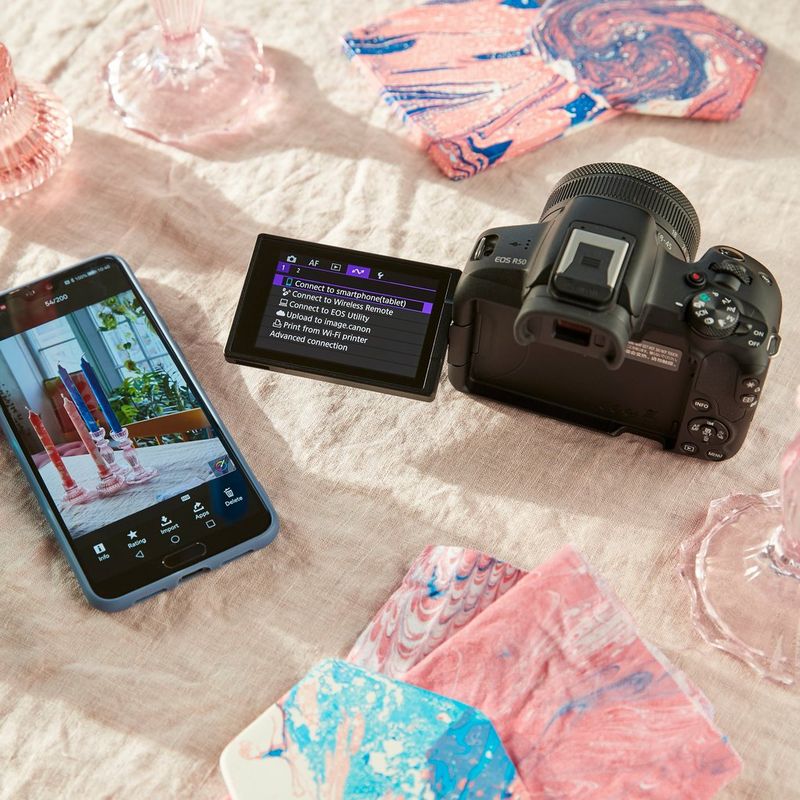 Canon EOS R50 Mirrorless Camera Body, Black Product kept besides a phone