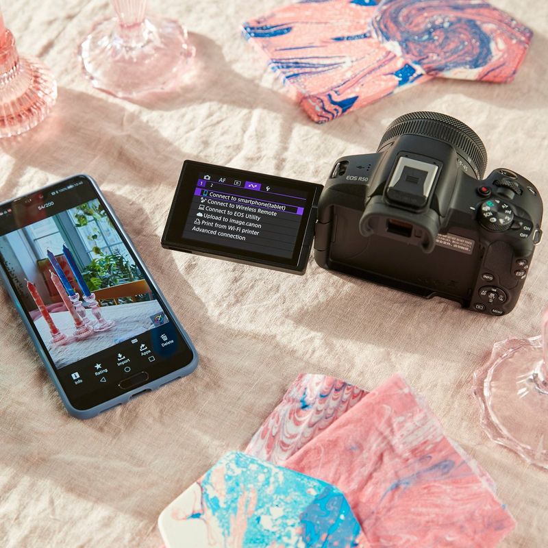 Canon EOS R50 Mirrorless Camera, Black + RF-S 18-45mm F4.5-6.3 IS STM Lens + Backpack + SD Card + Spare Battery Product kept besides a phone