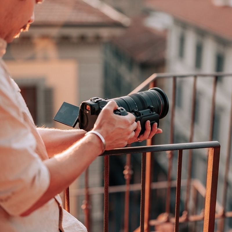 Adaptador de zoom motorizado Canon PZ-E2 Hombre mirando la pantalla de una cámara mientras el producto está acoplado a un objetivo