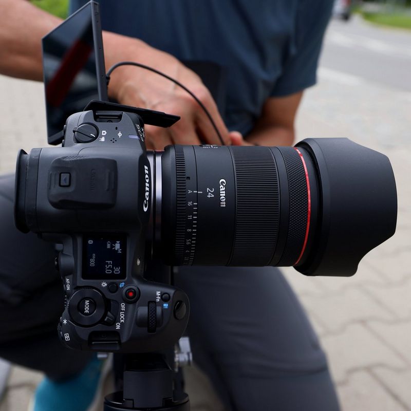Objectif Canon RF 24mm F1.4L VCM Homme prenant une photo avec un appareil photo et un objectif, l'objectif étant fixé à un trépied