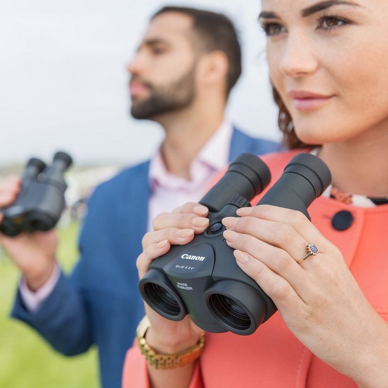 Canon 10x30 IS II Binoculars Man in the Background and Woman in the Foreground Both Looking Ahead and Holding the Binoculars Near their Faces