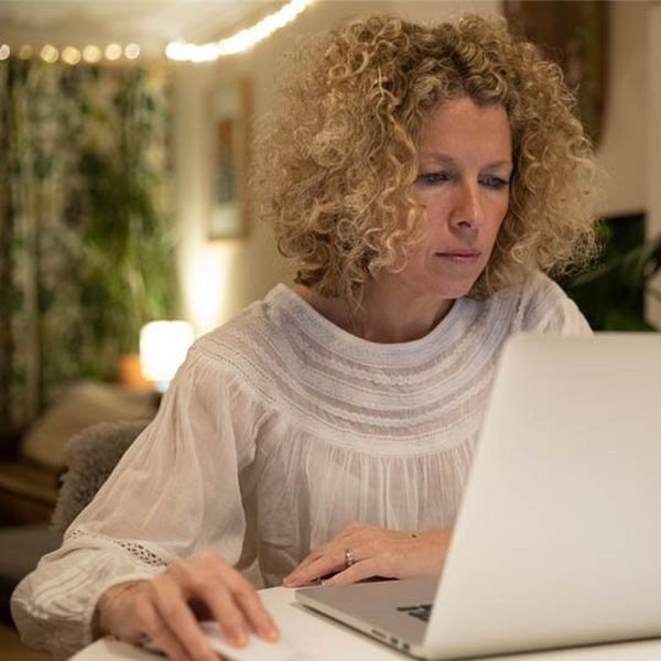 A blonde, curly-haired woman sits at a laptop.