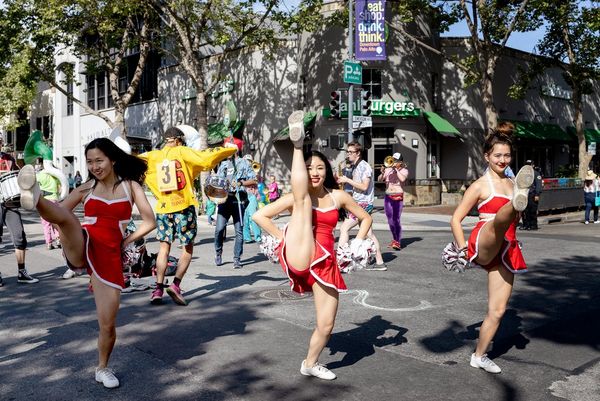 Three cheerleaders do high kicks in the middle of a street. Photo by Laura Morton.