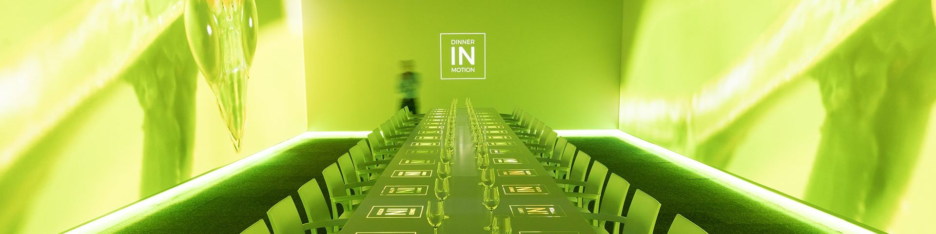A long dining table, bathed in green light with the Dinner in Motion logos projected onto it.