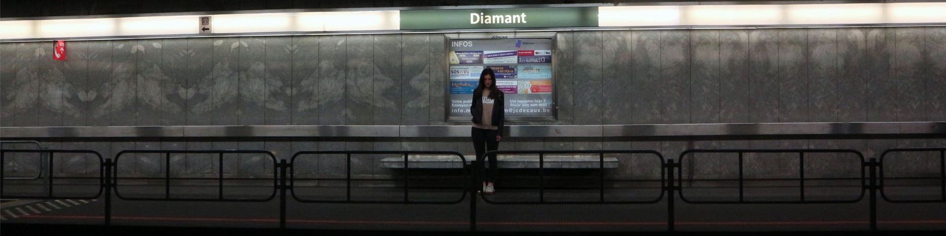 A young woman stands alone on a deserted metro platform.