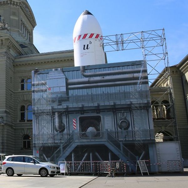 A building shaped like a rocket, sat in front of a building.