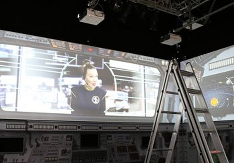 A ladder and projectors pointing to a screen, where a woman in a headset is broadcast.