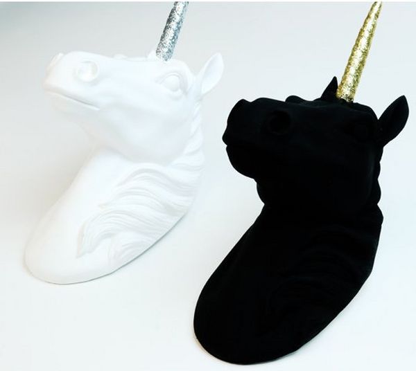 Two sculptures of unicorn heads, one in white and the other painted so black that it’s impossible to see the detail.
