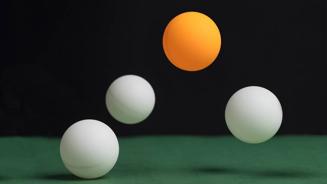 Balls bouncing on a table, one is orange the rest are white