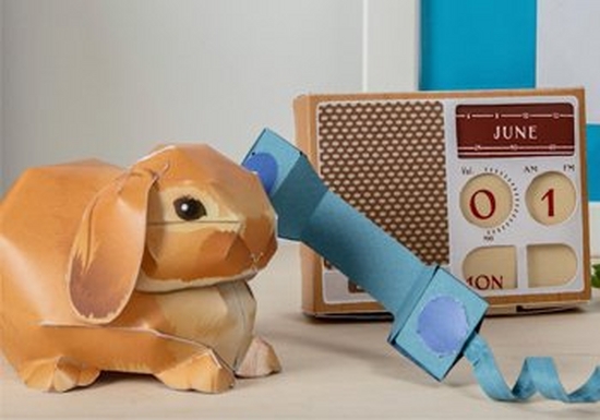 A 3D paper rabbit, talking on a paper telephone, with a paper radio in the background. 