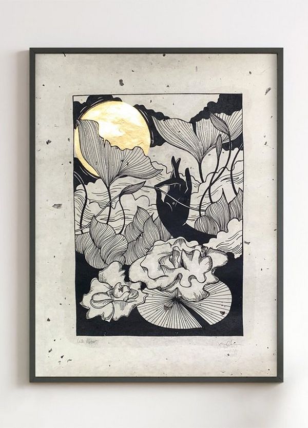 A black and white illustration in a black frame, against a wall. The picture is of finely drawn flowers and leaves, with a black hand in the centre, holding a stem. There is a gold leaf moon in the background.