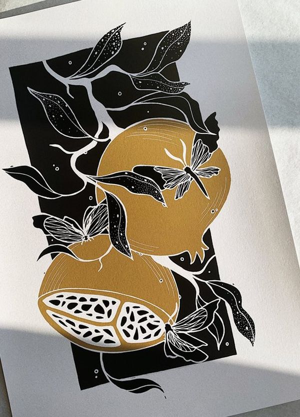 A black, white and gold illustration of figs and butterflies, printed on paper and lying flat.