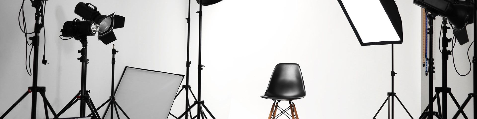 A black chair in the middle of a white photography studio, surrounded by lights.