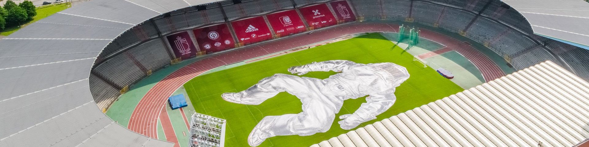 An aerial view of the King Baudouin Sports Stadium in Belgium, with a huge image of a figure wearing a silver fire-resistant suit laid out across the pitch.