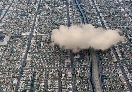 An aerial view of a city with a large white fluffy cloud above it on the right-hand side.