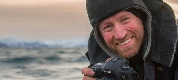 Photographer Audun Rikardsen smiles as he holds his camera by the sea.