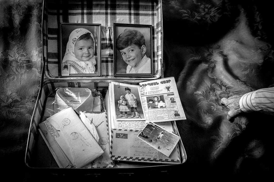 Inside a suitcase lid are photos of a young girl and boy. In the main suitcase is a shirt still in its plastic packaging, newspapers, letters and another photo of the children.