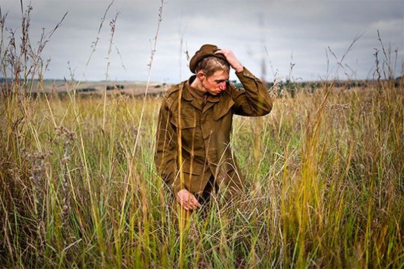 A group of white Afrikaans teenage boys wear army uniforms and stand in a group in front of an army tent, under a starry night sky.