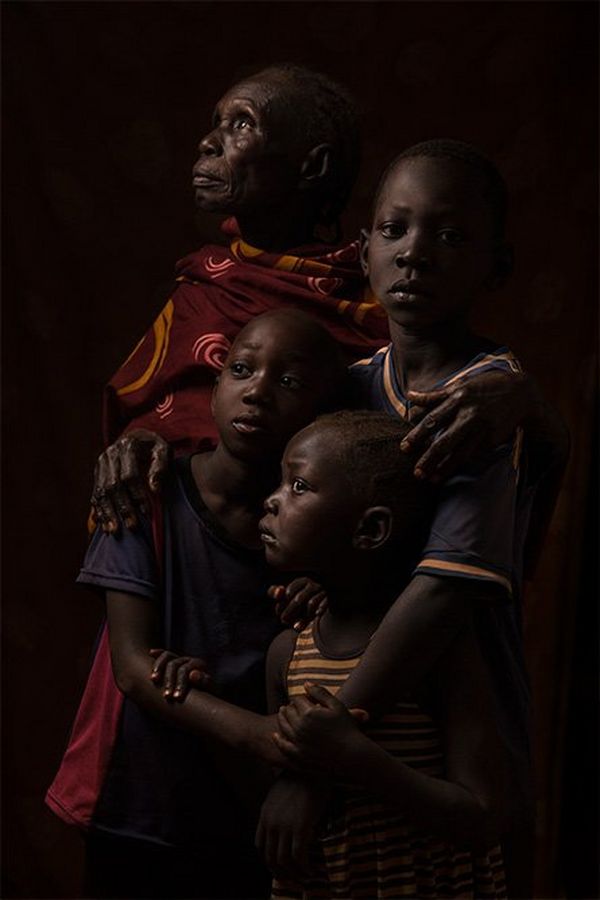 An African grandmother stands with her three grandsons in front of a dark background.