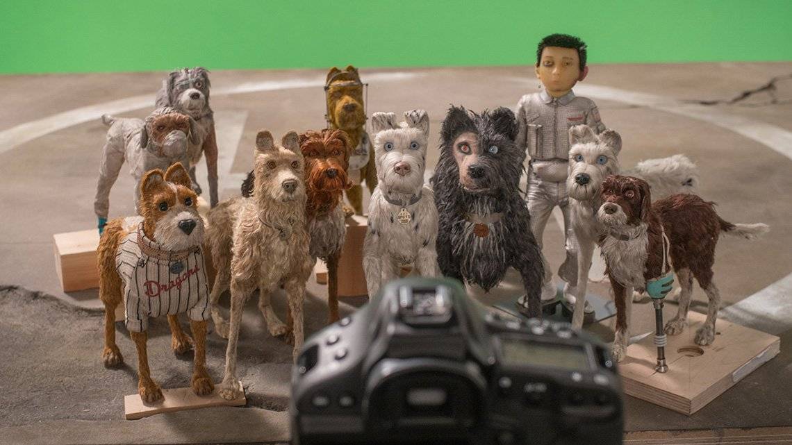 Dog puppets and an astronaut puppet are positioned in a group in front of a green screen, with a Canon EOS-1D X DSLR pointed at them to take their picture.