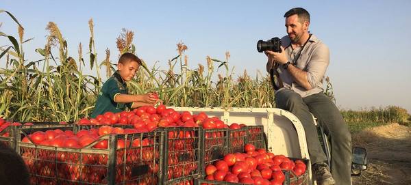 Photojournalist Ivor Prickett sits on the roof of a truck to take a picture of a boy sorting crates of tomatoes.