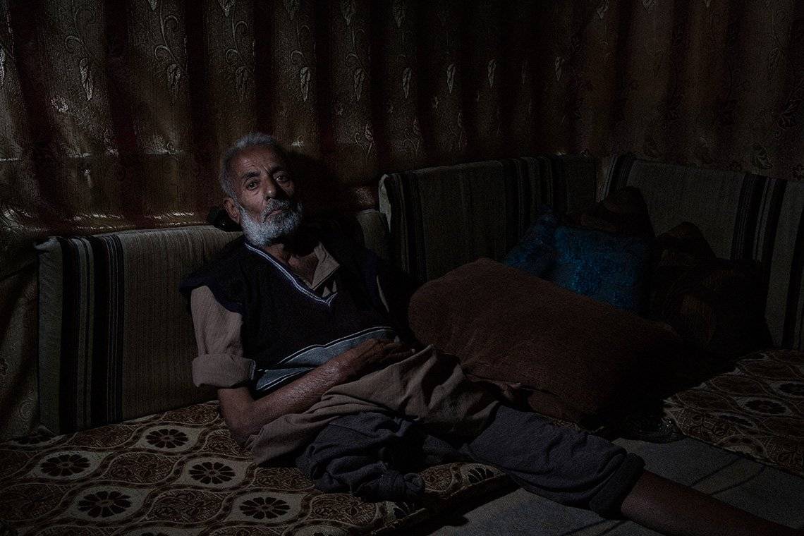 A man who has lost one legs leans against some cushions in a shabby makeshift tent in Lebanon. 