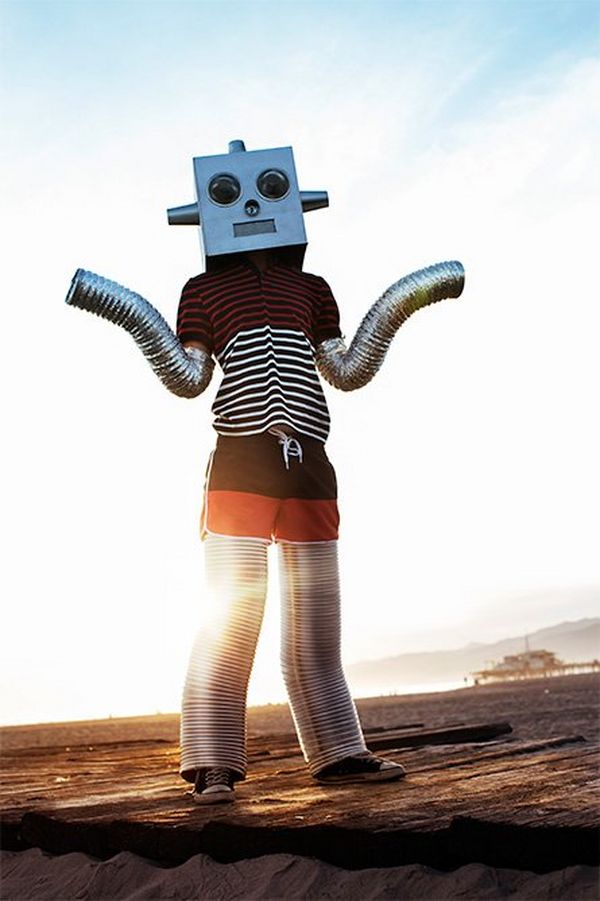 A person dressed as a robot stands on the ground outside, with the sun low on the horizon.