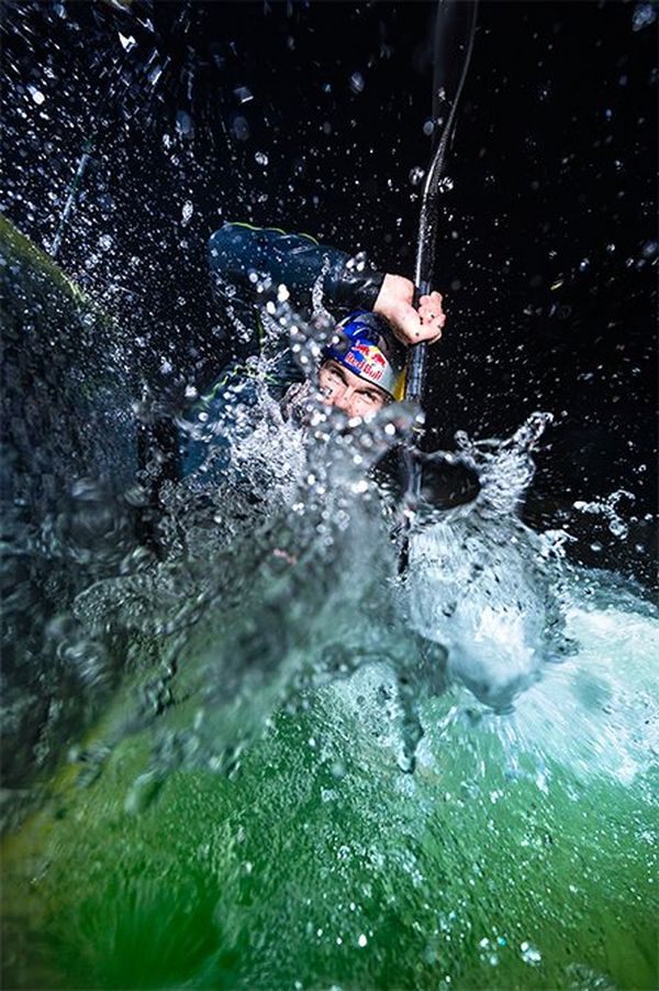 Kayaker Peter Kauzer is almost completely submerged in white water, paddle above his head, at night.
