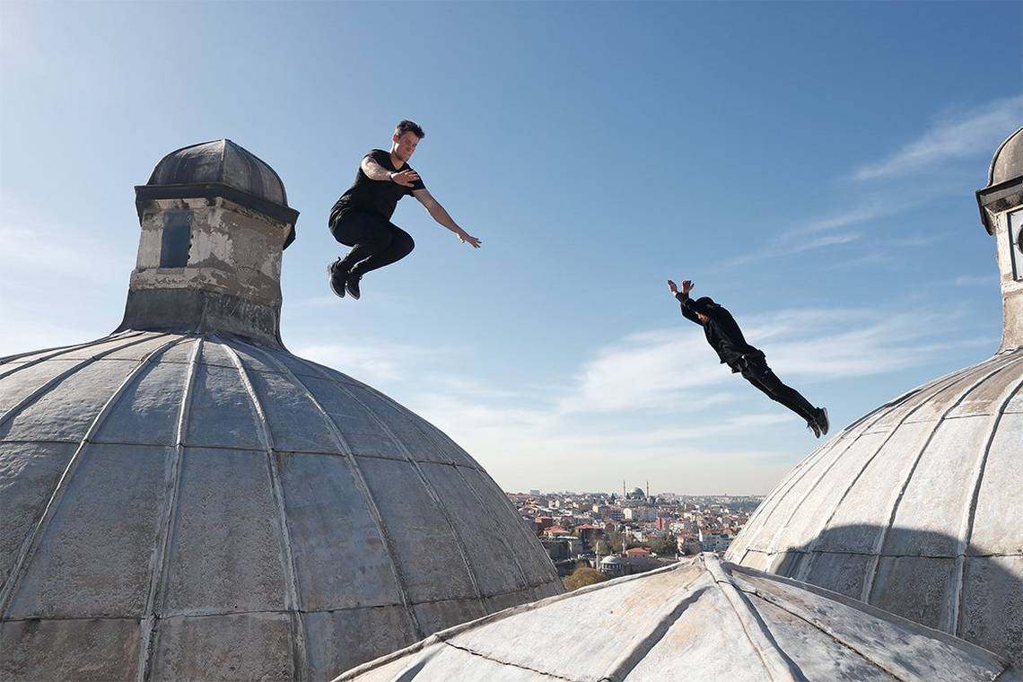 Two men leap in opposite directions on a domed roof in Istanbul.