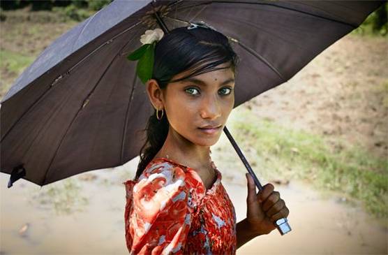 A young girl holding an umbrella stares at the camera.