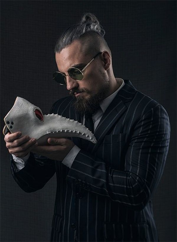 Wrestler Marty Scurll looks at a strange mask resembling an animal’s skull with a long beak.