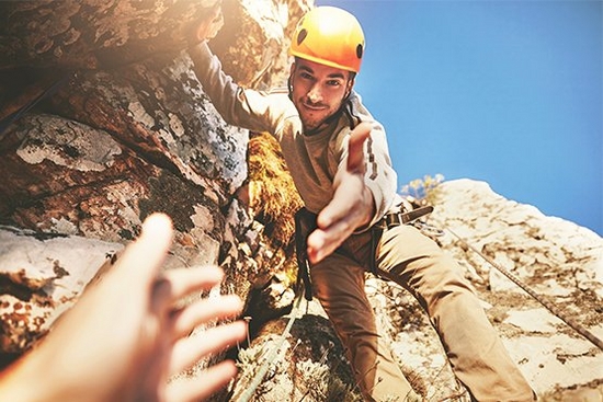 Rock climbing man leans down to take someone's hand