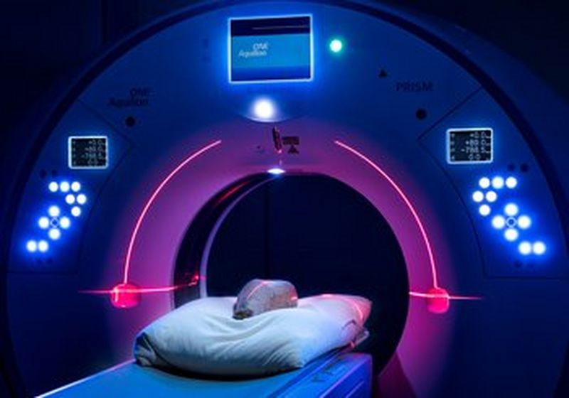 An object lies on a bed, inside a round CT scanner. It is illuminated with blue and purple lights.