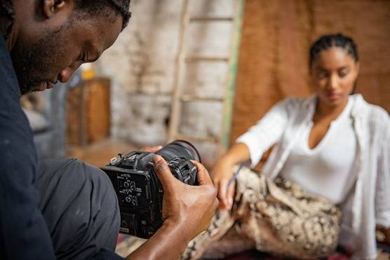 Jolade Olusanya holds a Canon EOS C70 camera to film a woman seated on the floor in front of him.